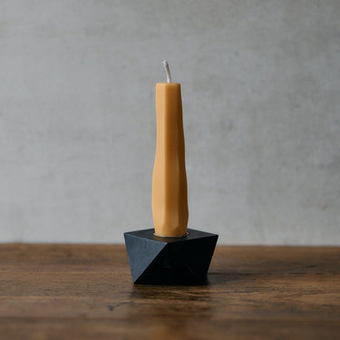 Tall, thin candle in a black holder on a wooden surface with a gray background