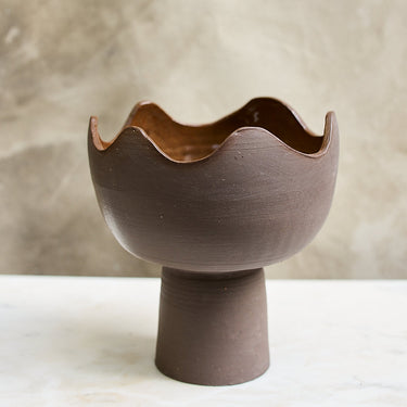 Ceramic bowl with wavy edge on a stand against a neutral background