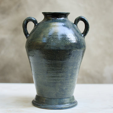 Black ceramic vase with handles on a white surface and beige background