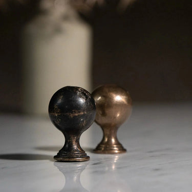 Two metallic knobs, one black and one bronze, on a reflective surface with a blurred background.