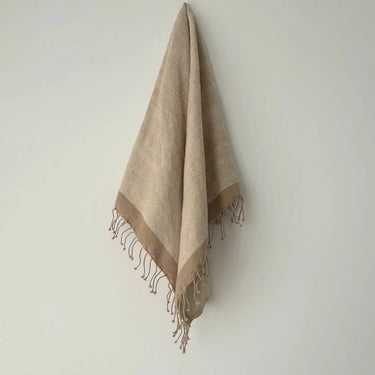 Beige towel with fringes hanging on a light gray wall