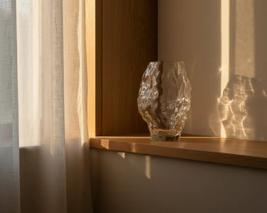 Glass vase on a wooden shelf with soft lighting and shadows