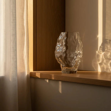 Glass vase on a wooden shelf with soft lighting and shadows