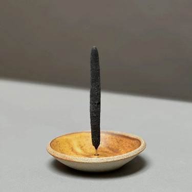 Ceramic incense holder with a single incense stick on a neutral background