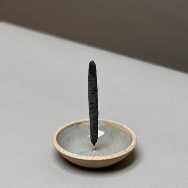 Incense stick in a small ceramic holder on a neutral background