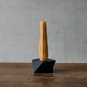 Tall, thin candle in a black holder on a wooden surface with a gray background