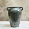 Green ceramic vase with two handles on a white surface and beige background