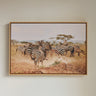 Framed artwork of zebras in a savannah setting on a wall.