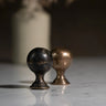 Two metallic knobs, one black and one bronze, on a reflective surface with a blurred background.