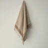 Beige towel with fringes hanging on a light gray wall